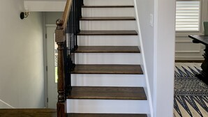 Eine Treppe mit Holzboden und einem schwarzen Geländer, die zu einer Zwischenebene mit einem Blumentopf führt.