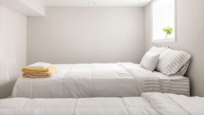 Ein schlicht eingerichtetes Schlafzimmer mit einem Bett, einem Fenster mit Pflanze und einem ordentlich bezogenen Bett mit zusammengelegten Handtüchern.