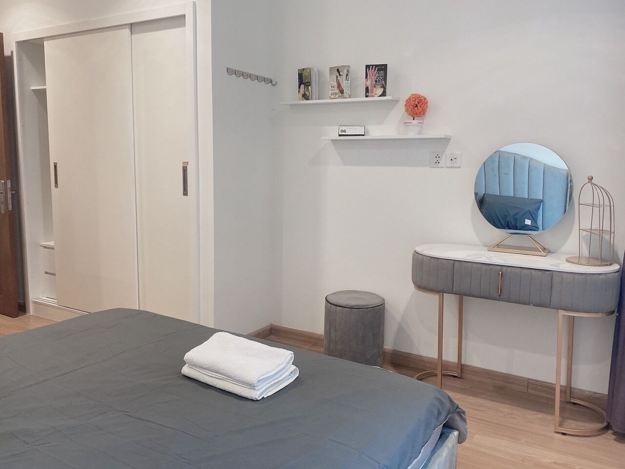 Ein Schlafzimmer mit einem Bett, einem Schminktisch mit Spiegel und einem Regal mit Büchern und einer Vase.