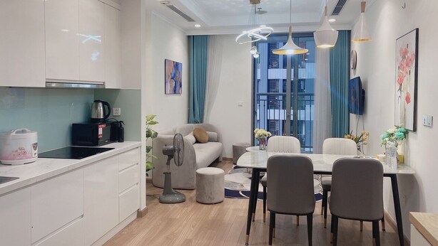 A modern kitchen with white cabinets, a dining area with a round table and chairs, and a large window with blue curtains.