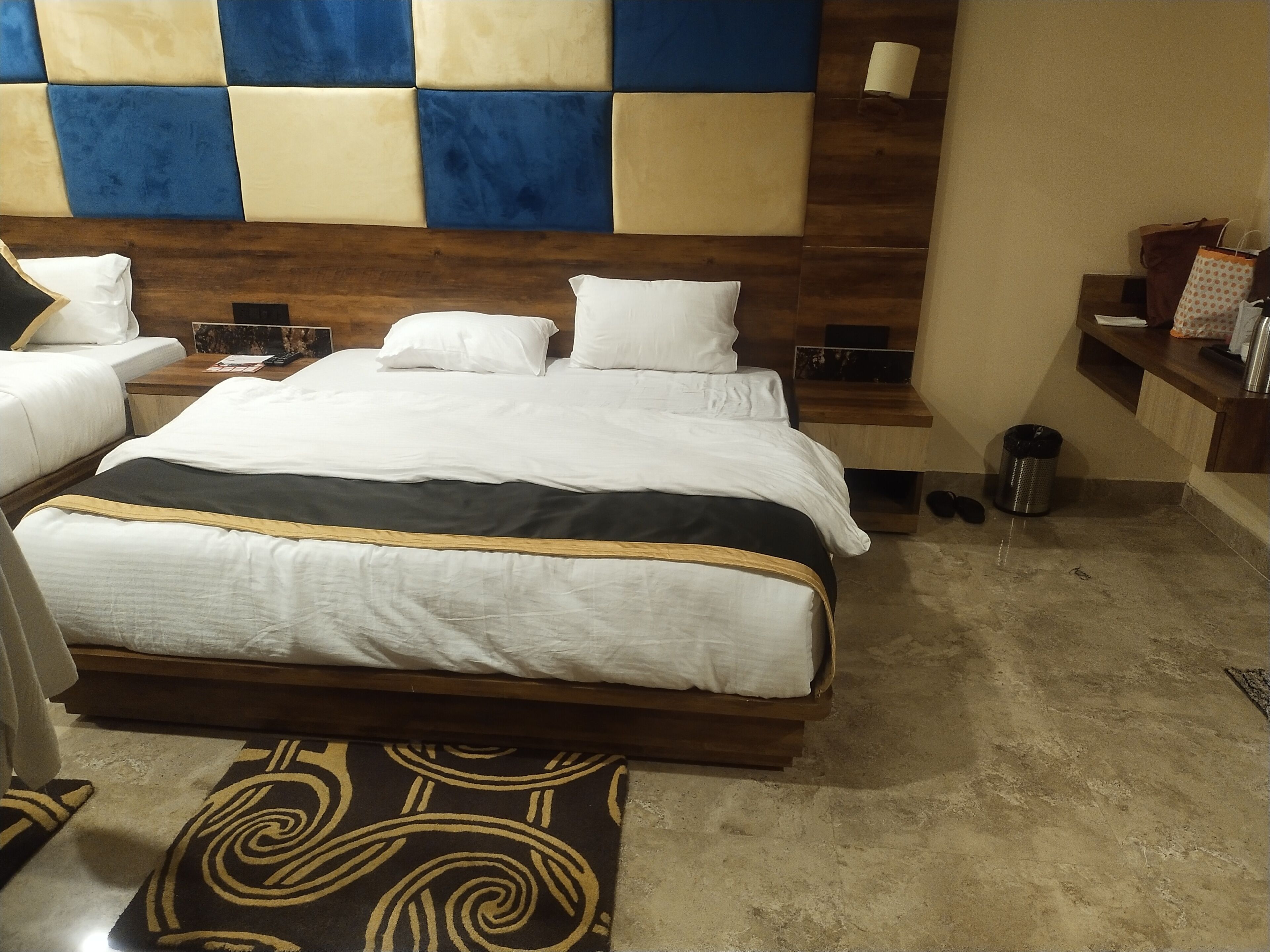 A hotel room with a large bed, a wooden headboard, a small desk, and a trash can.