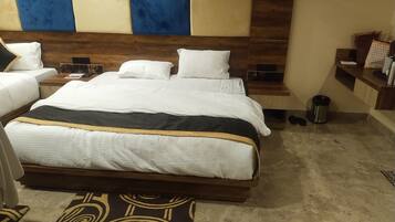 A hotel room with a large bed, a wooden headboard, a small desk, and a trash can.