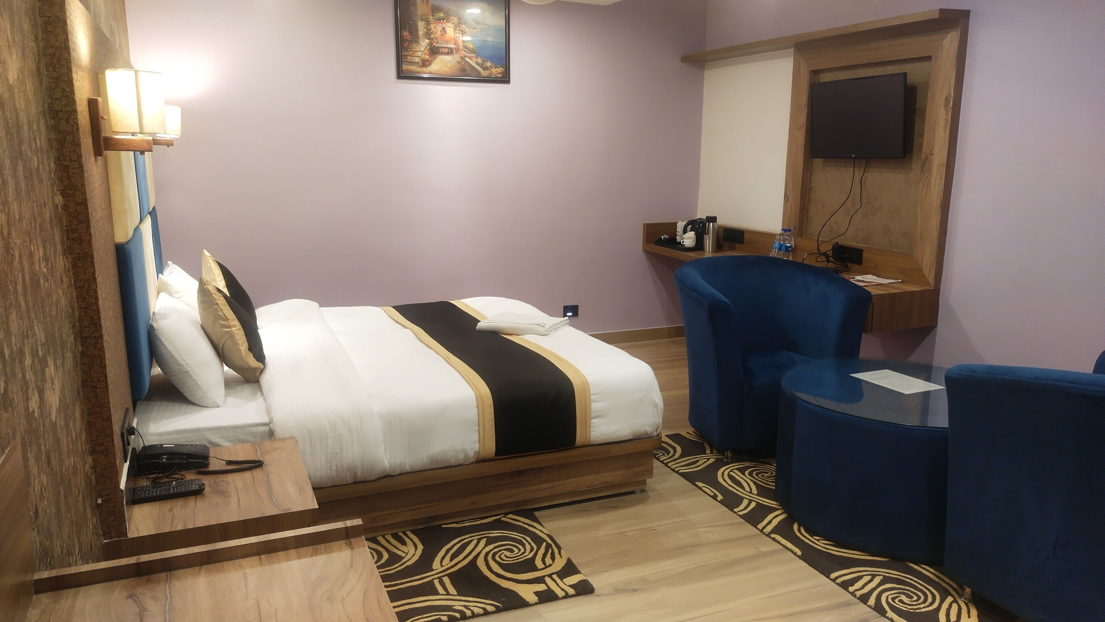 A hotel room with a bed, a desk, a chair, a TV, and a painting on the wall.