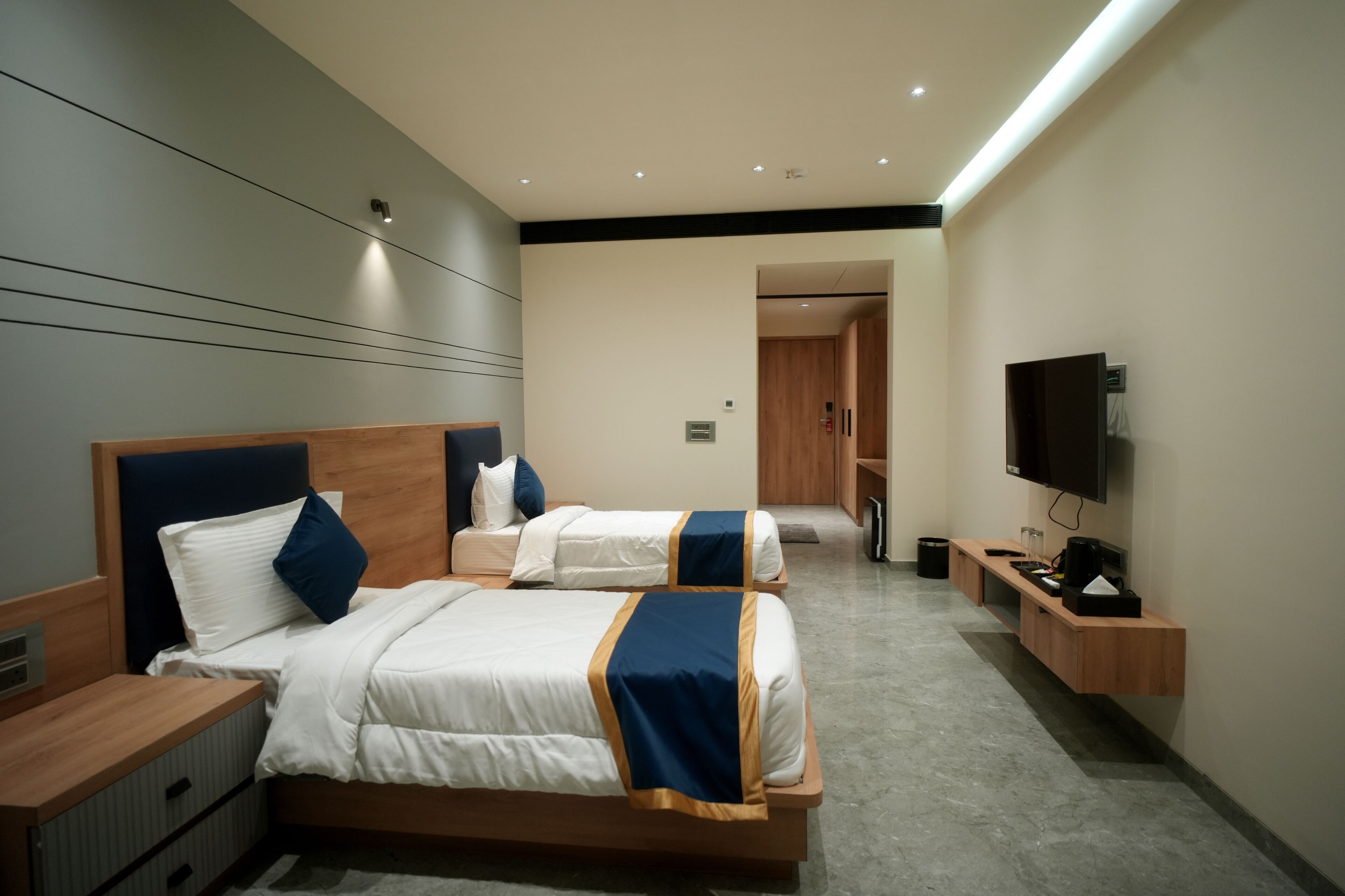 A hotel room with two beds, a TV, a desk, and a bathroom.