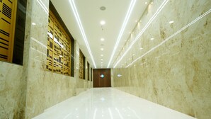 A long, well-lit hallway with marble walls and a shiny floor, leading to a door at the end. - Dream Inn By Spring Tree (Wadhwan)