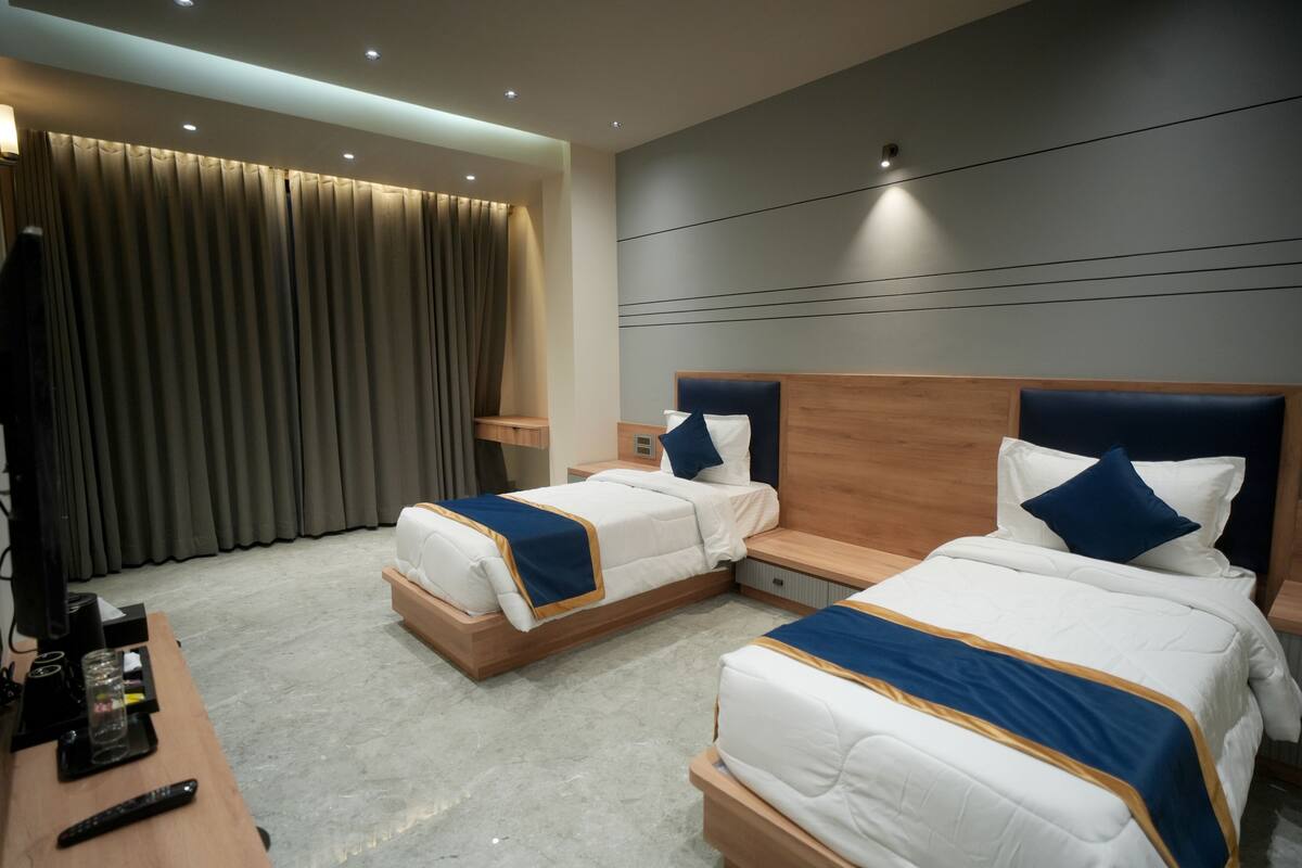 A hotel room with two beds, a desk with a remote control, and a TV.