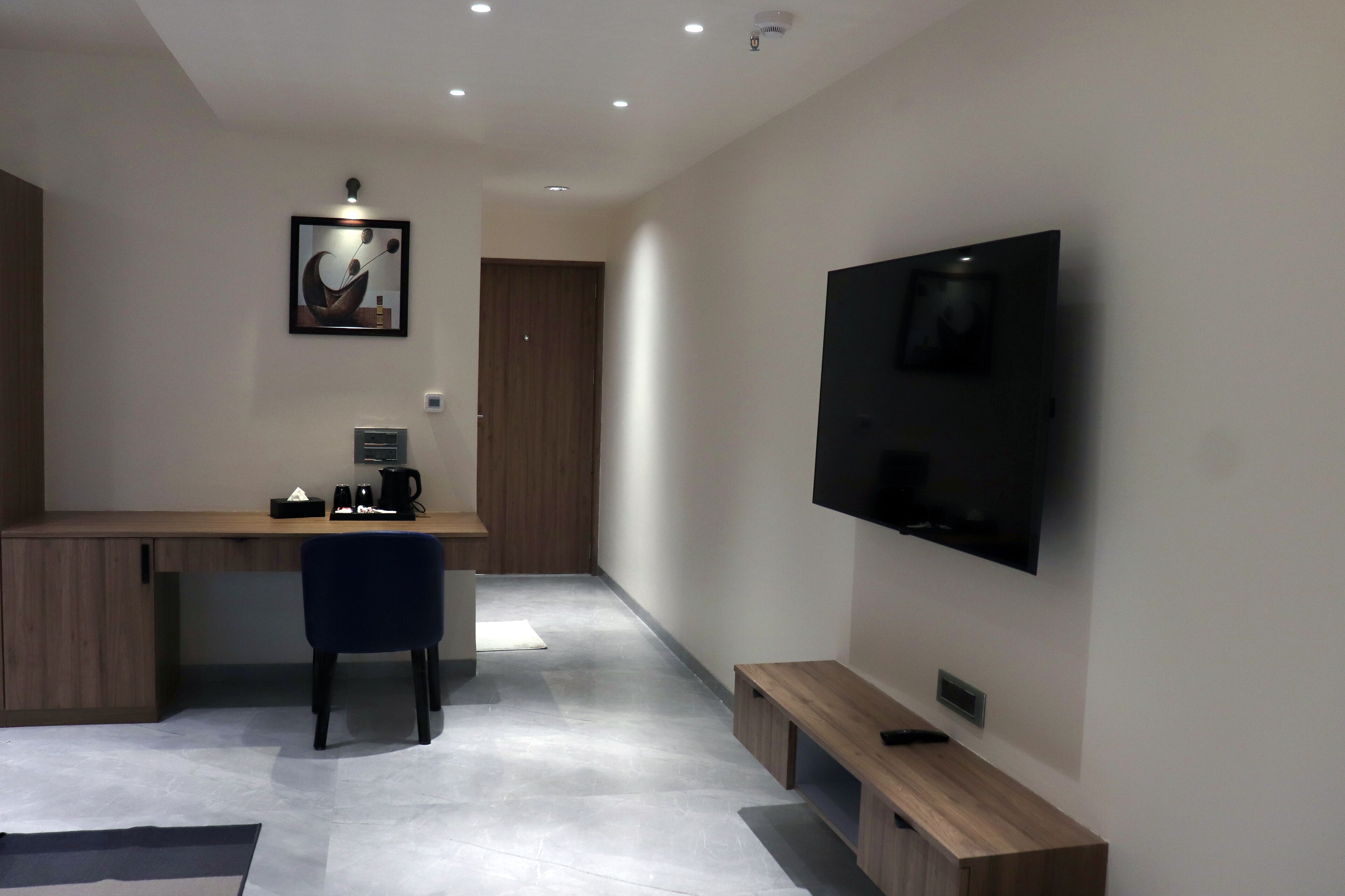 Habitación moderna y bien iluminada con un escritorio de madera, una silla, un televisor de pantalla plana en la pared y un banco.