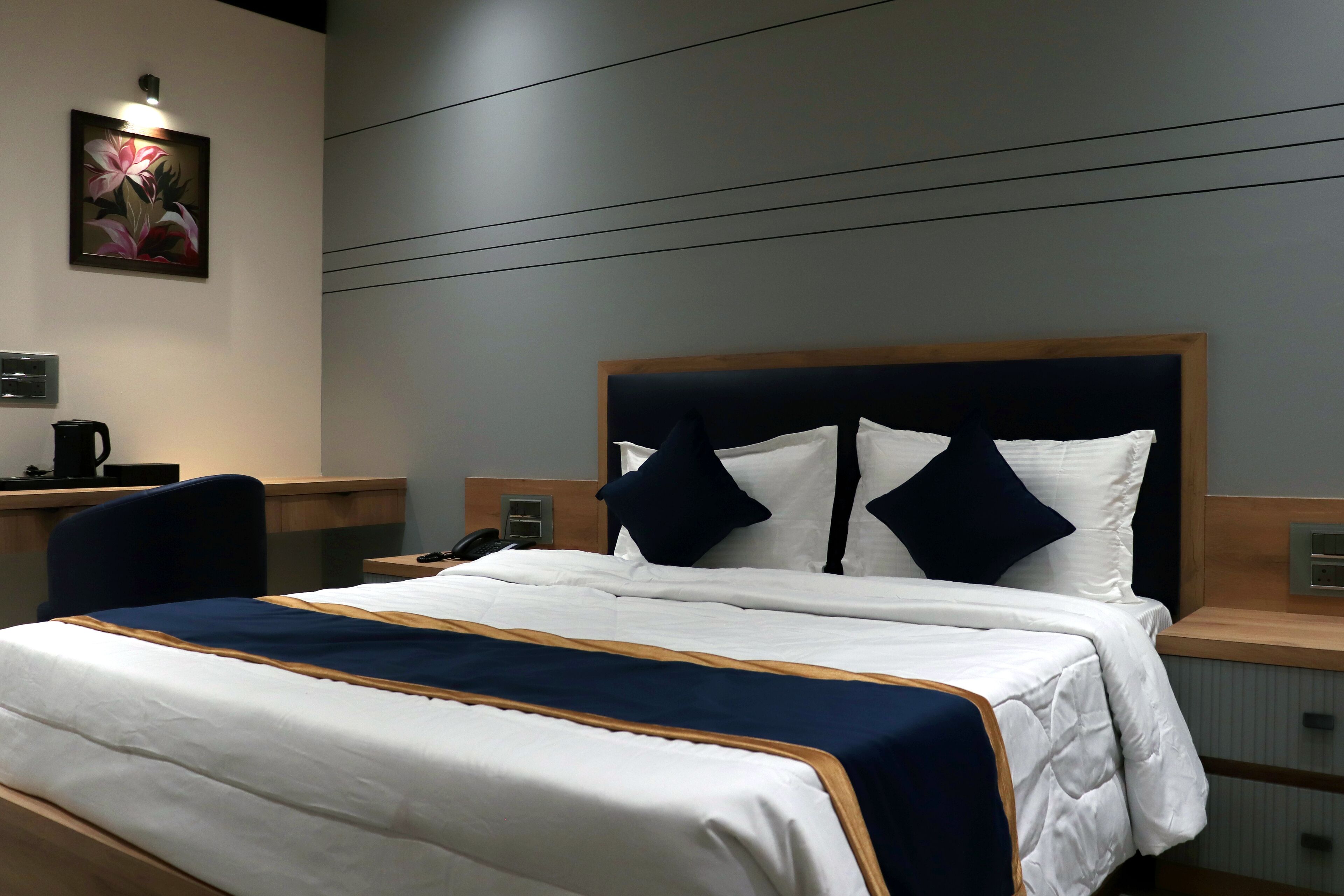A neatly made bed with a white and navy blue bedspread, a wooden headboard, and two bedside tables with lamps.