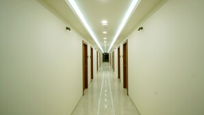 A long, well-lit hallway with doors on both sides, leading to rooms. - Dream Inn By Spring Tree (Wadhwan)