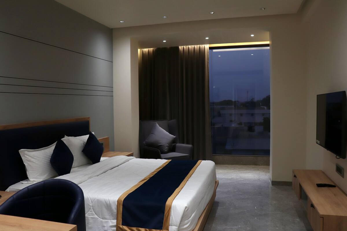 A modern hotel room with a large bed, a TV, a desk, and a chair.