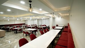 A spacious dining area with long tables and red chairs, featuring a modern ceiling design with recessed lighting. - Dream Inn By Spring Tree (Wadhwan)