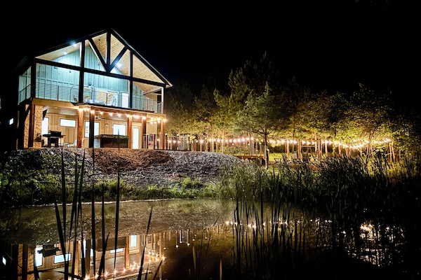 Cozy lakeside cabin glowing with string lights, reflecting on the water at night