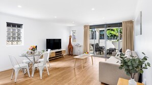 A modern living room with a dining area, a sofa, a television, and a giraffe statue. - Central 2BR APT for 6PPL, w/ free parking@SouthBNE (South Brisbane)