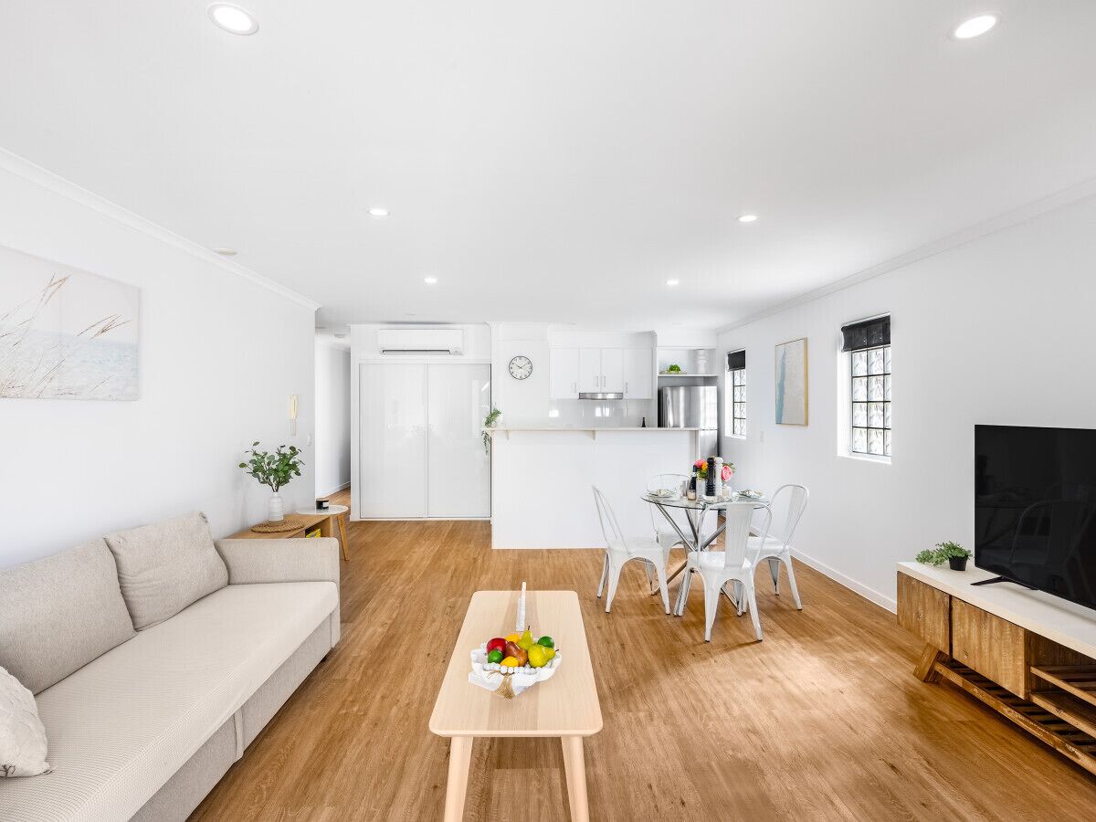 A modern living room with a sofa, dining table with chairs, a TV, and a kitchen area in the background.