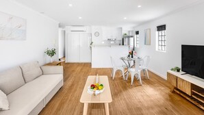 A modern living room with a sofa, dining table with chairs, a TV, and a kitchen area in the background. - Central 2BR APT for 6PPL, w/ free parking@SouthBNE (South Brisbane)