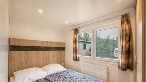 Une chambre à coucher avec une tête de lit en bois, une grande fenêtre avec des rideaux et un radiateur.