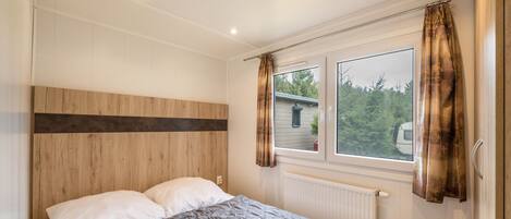 Un dormitorio con cabecera de madera, un ventanal con cortinas y un radiador.