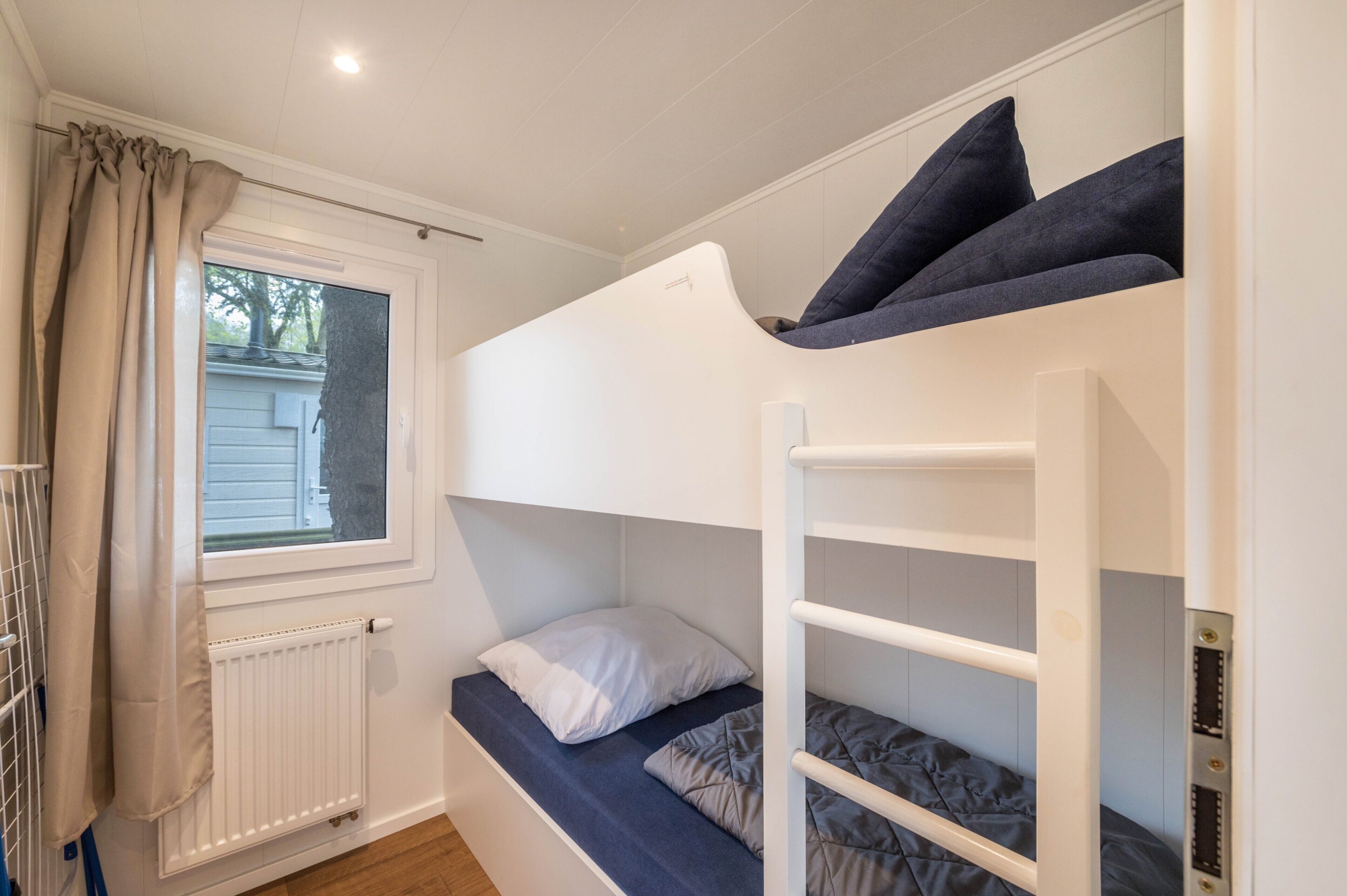 A bunk bed room with a window, radiator, and a curtain.