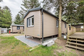 A single-story mobile home with a front deck, a small porch, and a window. - Apartment 'Tiny House Lohmen Garder See' with Private Terrace and Wi-Fi (Lohmen)