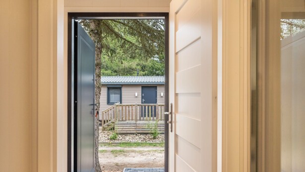 Une porte d’entrée donnant sur un bâtiment doté d’une terrasse en bois et d’un petit jardin.