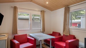 Une pièce avec un plafond en bois, deux fenêtres avec des rideaux, une table et des sièges rouges.
