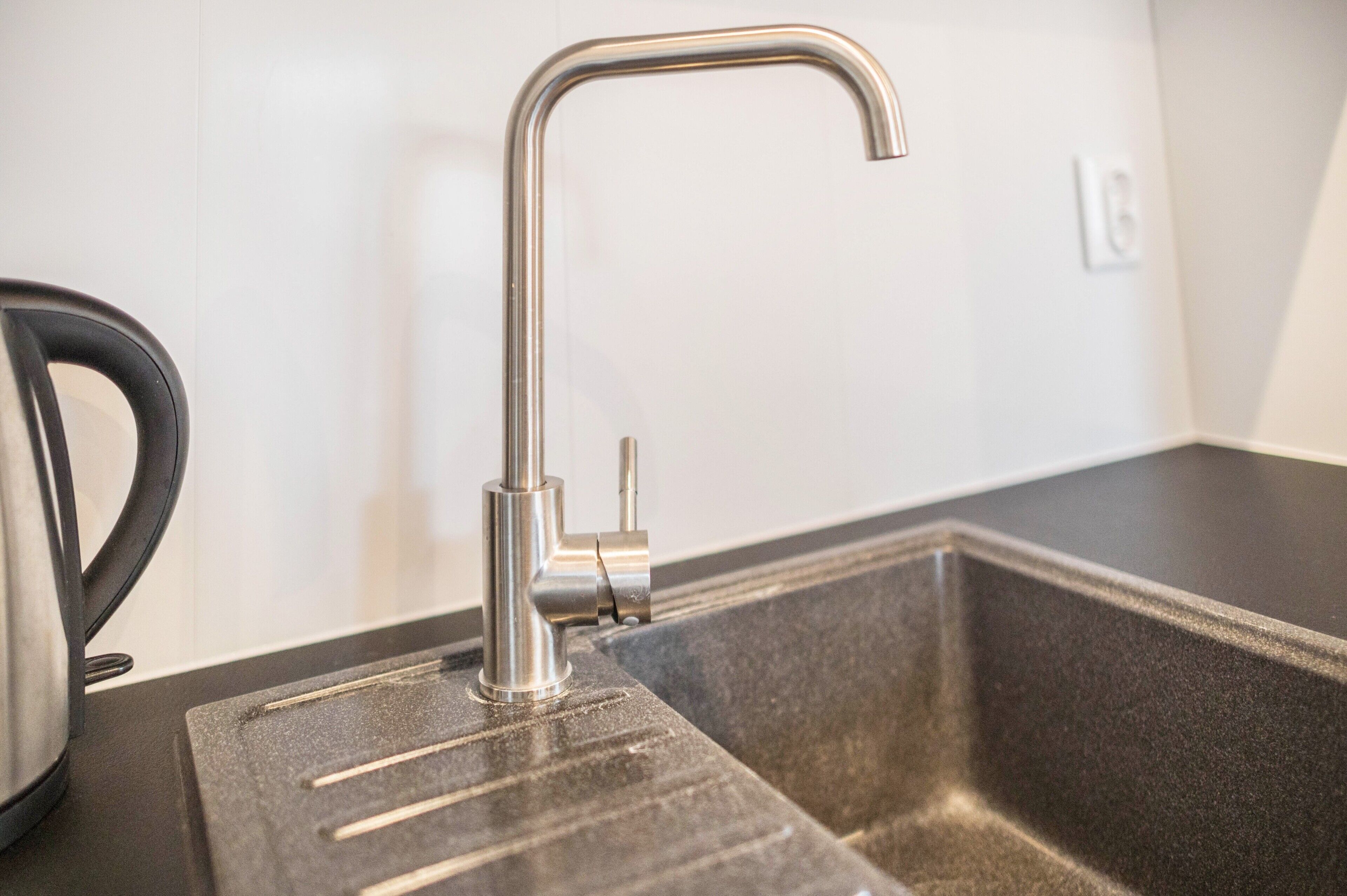 A kitchen sink with a modern faucet and a kettle on the counter.