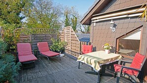 An outdoor deck with a table and chairs, a wooden fence, and a building with a window.