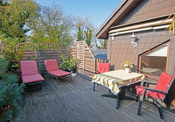 Une terrasse extérieure avec une table et des chaises, une clôture en bois et un bâtiment doté d’une fenêtre.