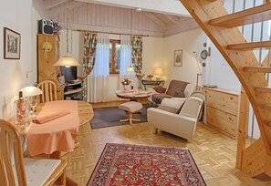 Un salon chaleureux avec un plancher en bois, un canapé, une table à manger avec des chaises, un petit tapis et un escalier.