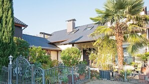 A residential building with a tiled roof, a covered porch, and a fenced garden area with potted plants and a palm tree.