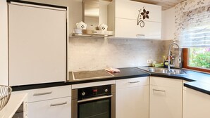 A kitchen with white cabinets, a stainless steel oven, a black countertop, and a window with a view of greenery.