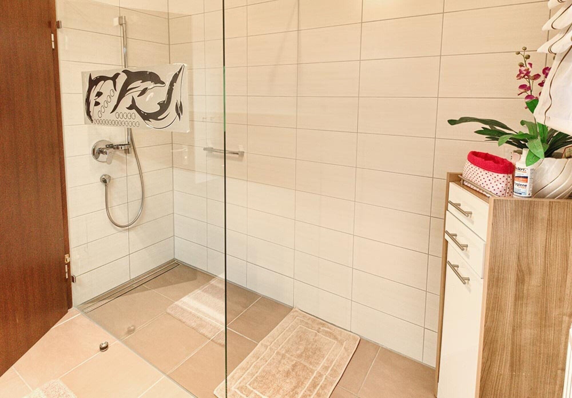 A bathroom with a glass shower enclosure, a wooden cabinet with drawers, and a potted plant.