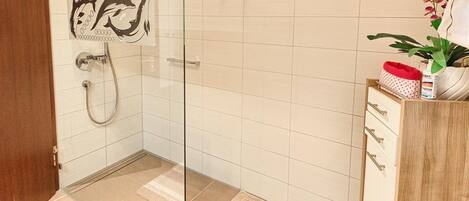 A bathroom with a glass shower enclosure, a wooden cabinet with drawers, and a potted plant.