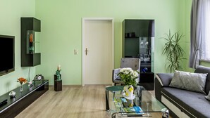 A living room with a flat-screen TV, a sofa, a coffee table, and a bookshelf. - Apartment "Burgblick" with Mountain View, Shared Terrace & Wi-Fi (Plaue)