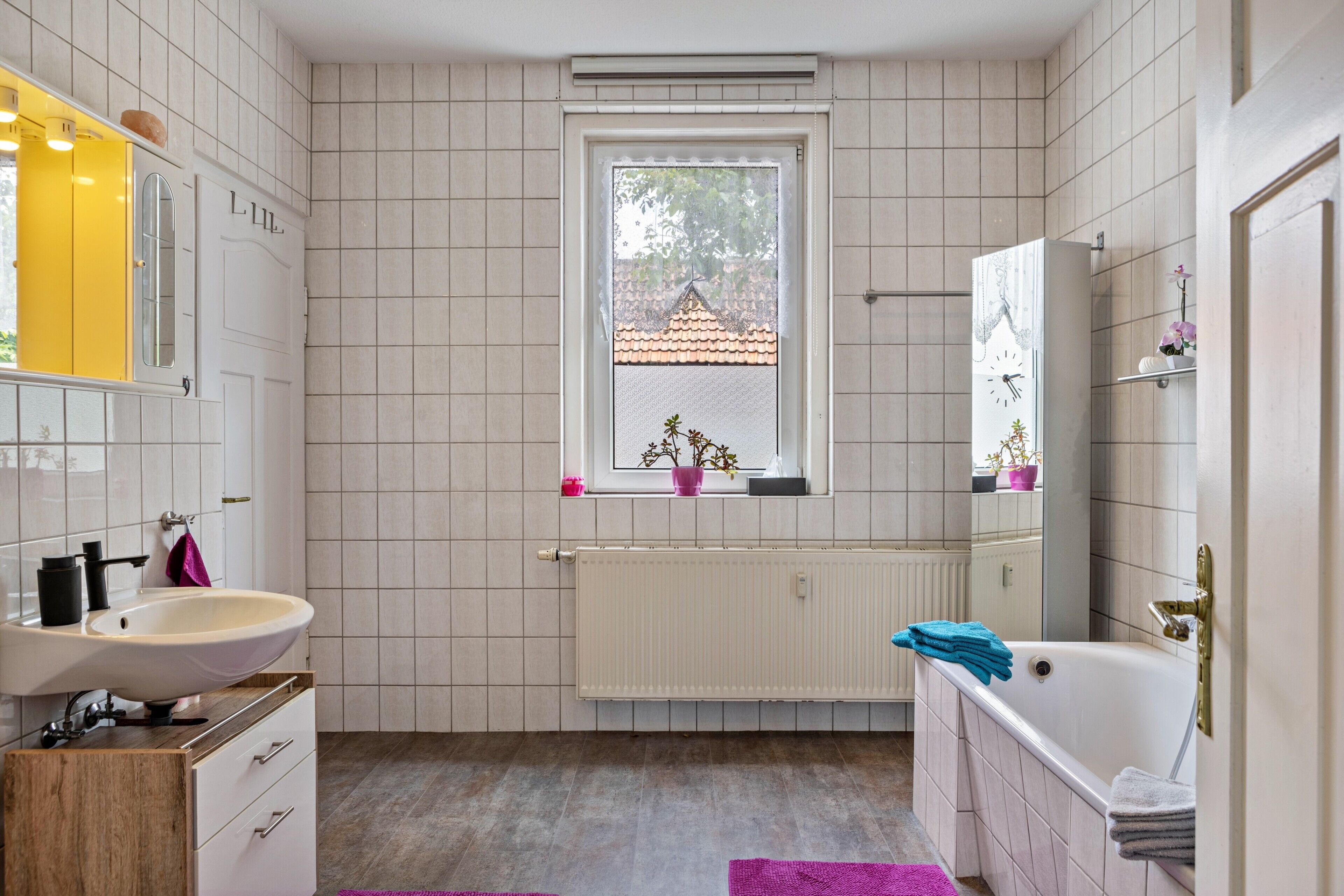 Un baño con lavamanos blanco, bañera, ventana con vistas y espejo.