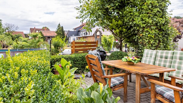A patio with a wooden table and chairs, surrounded by lush greenery and a view of houses. - Apartment "Burgblick" with Mountain View, Shared Terrace & Wi-Fi (Plaue)