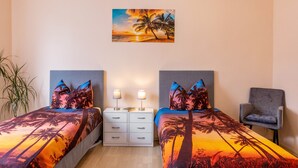 A bedroom with two beds, a nightstand, a chair, and a painting of a sunset over palm trees. - Apartment "Burgblick" with Mountain View, Shared Terrace & Wi-Fi (Plaue)