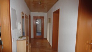 Un passadís amb terres de fusta, una porta amb un panell de vidre mat i un armari de fusta amb un telèfon.