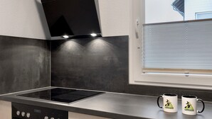 A kitchen with a black range hood, stainless steel countertop, and two mugs on the windowsill. - Apartment 'Hexe 4 ' with Balcony and Wi-Fi (Braunlage)