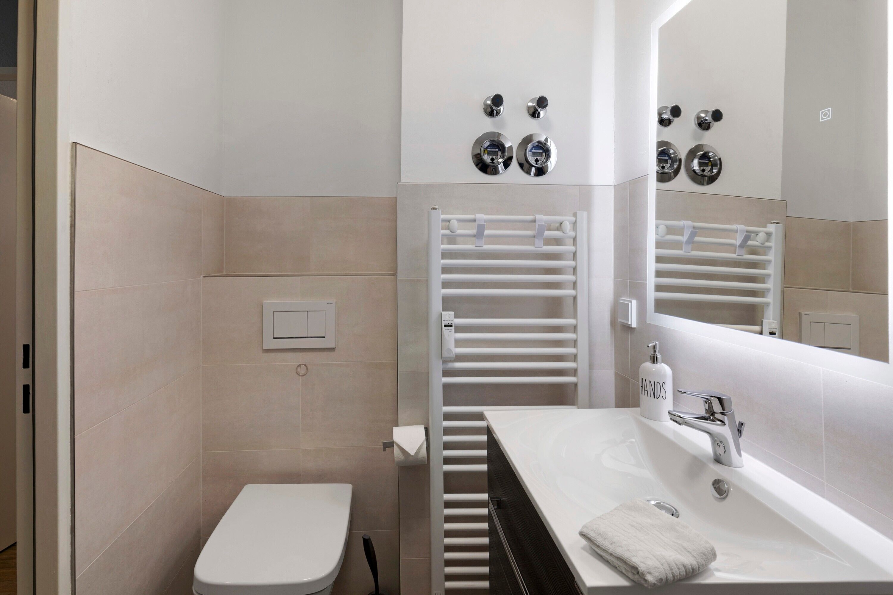 Un baño moderno con inodoro, lavamanos con espejo y un perchero para toallas.