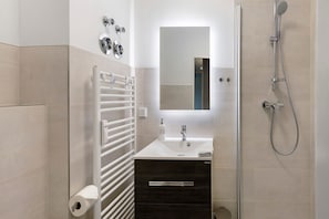 Un baño moderno con lavamanos blanco, un espejo, toallero y ducha.