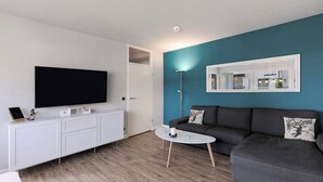 A modern living room with a flat-screen TV, white cabinetry, a grey sofa, and a round coffee table. - Apartment 'Hexe 4 ' with Balcony and Wi-Fi (Braunlage)
