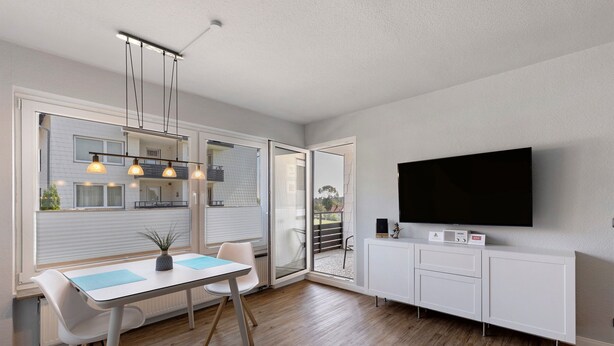 A modern kitchen with a dining area, a TV mounted on the wall, and a sliding glass door leading to an outdoor patio. - Apartment 'Hexe 4 ' with Balcony and Wi-Fi (Braunlage)