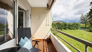 Een balkon met een stoel, een tafel en uitzicht op een groen landschap.