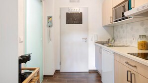 Een smalle keuken met een witte deur, een magnetron, een spoelbak en een pot pasta op het aanrecht.