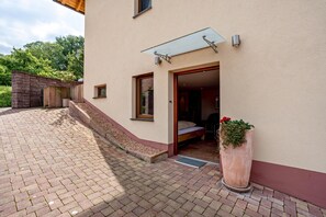 Un bâtiment doté d’un patio, d’une entrée avec porte vitrée, d’un petit espace extérieur aménagé avec des sièges et d’un pot de fleurs.