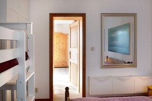 Une chambre avec des lits superposés, une porte en bois donnant sur un couloir et un miroir orné d’un tableau.