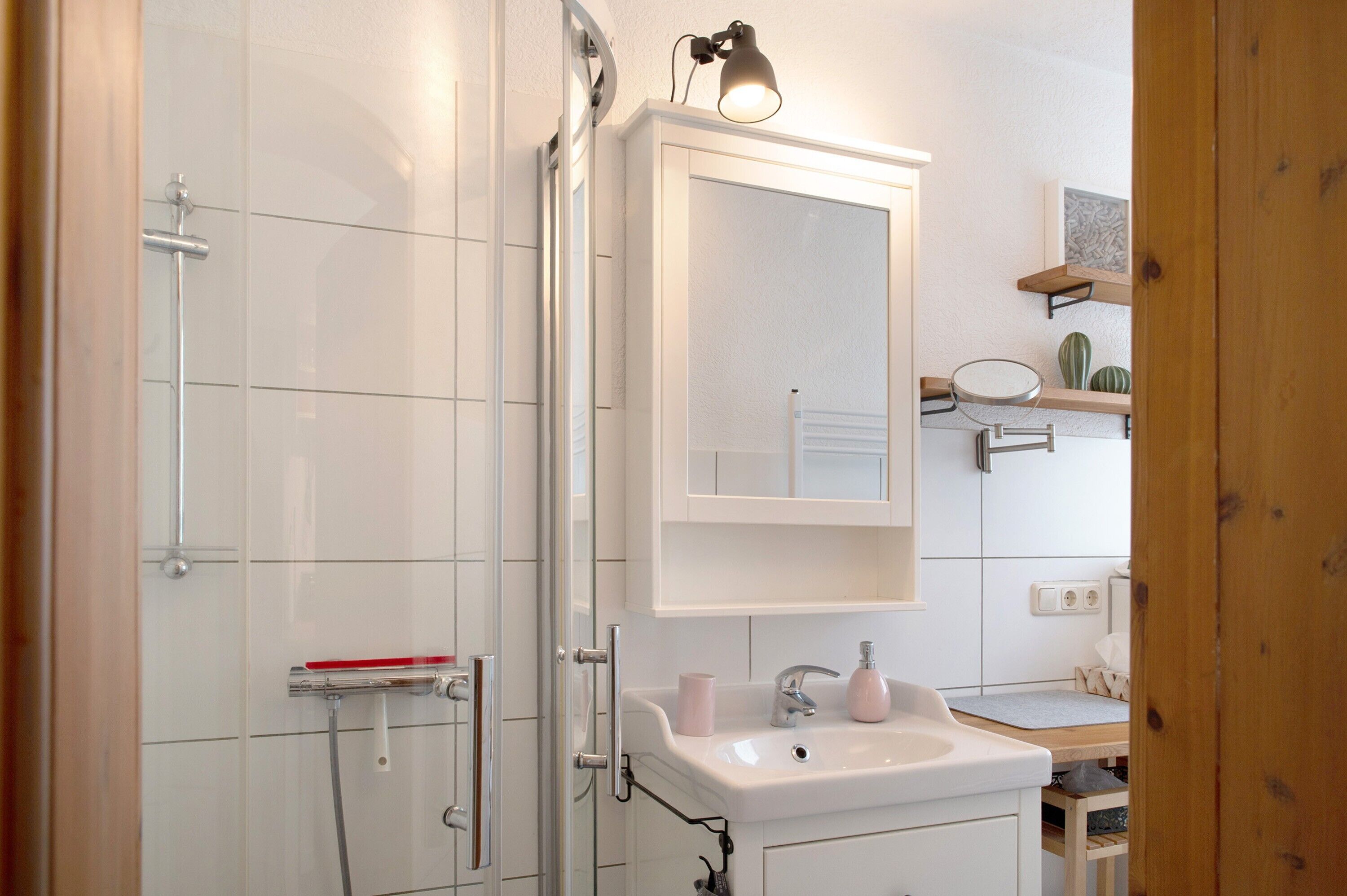 Een badkamer met een douche, wastafel, spiegel en een plank met decoratieve objecten.