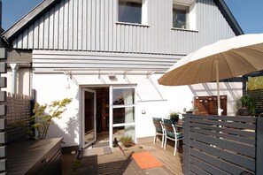 Une maison à l’extérieur blanc, dotée d’une terrasse en bois, d’une porte-fenêtre coulissante et d’un parasol.