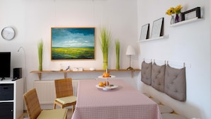 A room with a dining table, chairs, a painting, a clock, and a shelf with decorative items.